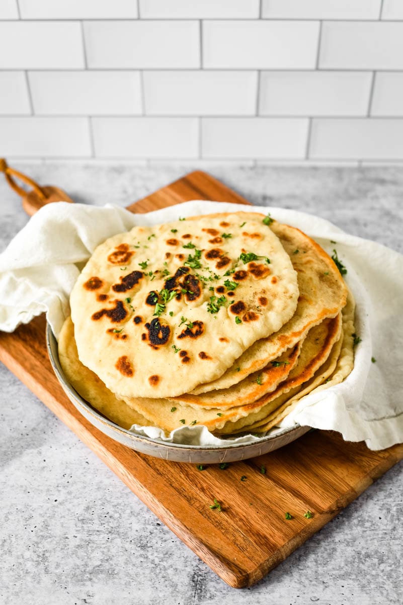 stack of sourdough naan in dish on wood board