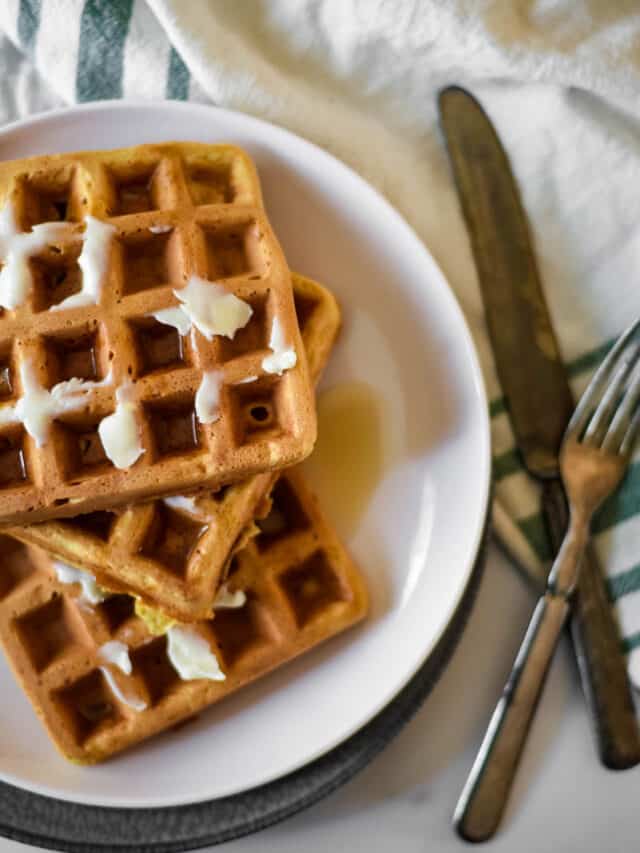overhead view of plate of sourdough waffles with butter and syrup. Fork and knife beside plate.