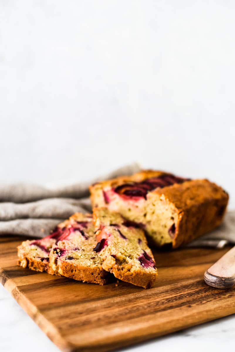 plum and sourdough quick bread loaf on wooden cutting board with three slices laying in front