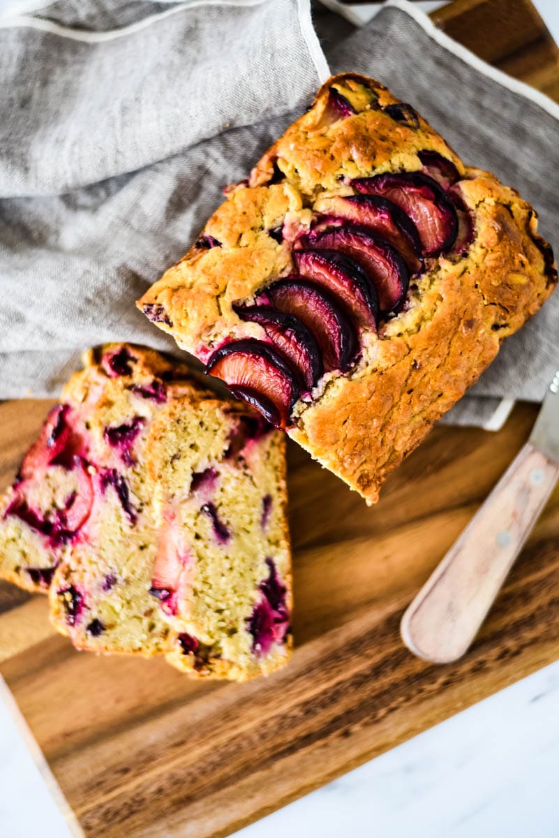 loaf of sourdough quick bread with plums, slices and knife beside