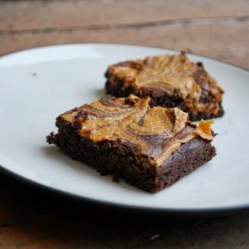 Two swirled chocolate stout peanut butter brownies sitting on a white plate on a wooden table