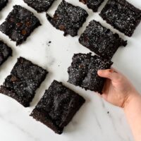 A toddler holding a black bean brownie with other black bean brownies sitting on the white marble countertop