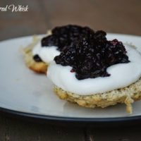 two earl grey scones on white plate with devonshire cream and blueberry preserves on top