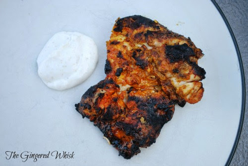 grilled tandoori chicken thighs on a plate next to raita sauce
