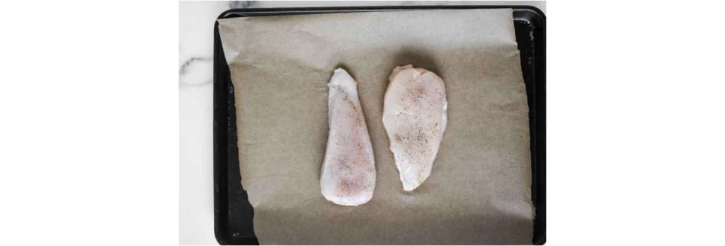 chicken breasts seasoned with salt and pepper on baking sheet lined with parchment paper