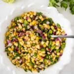 sweet corn salsa in white bowl with lime and cilantro beside bowl