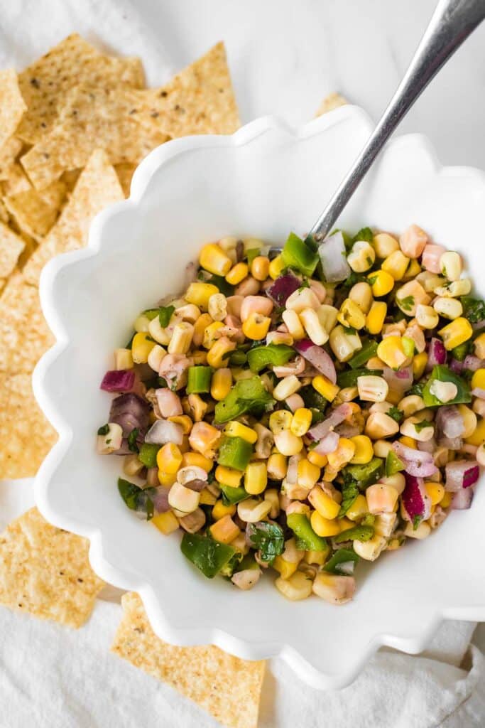 corn salsa in white bowl surrounded by tortilla chips
