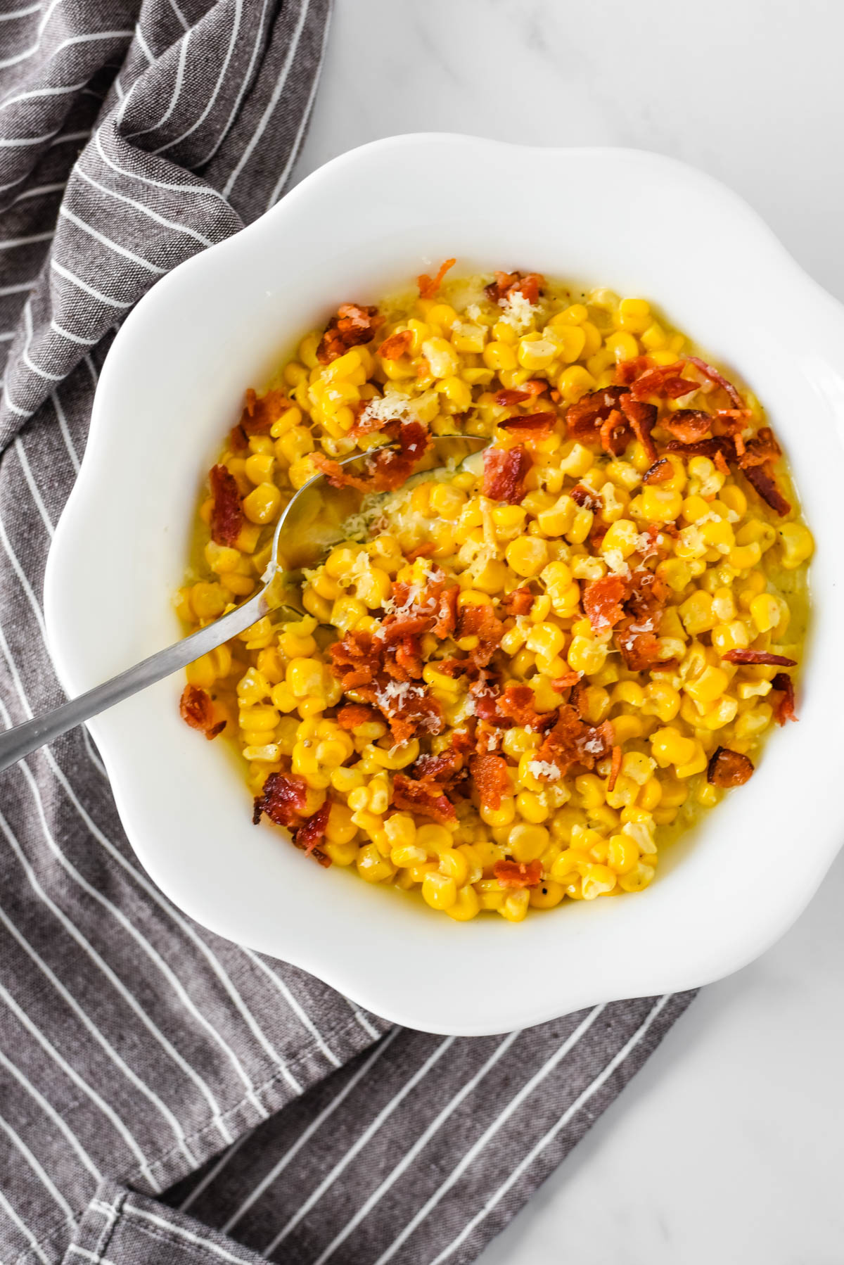 creamed corn with bacon in white bowl with spoon