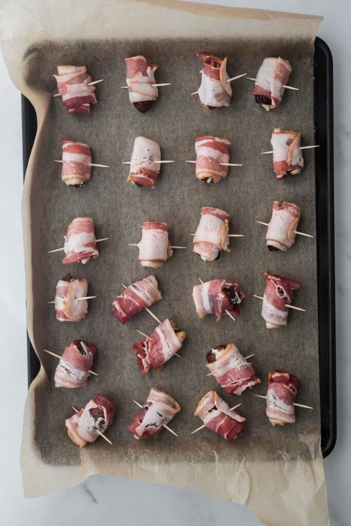 dates wrapped in bacon and secured with toothpick lined on baking tray with parchment paper