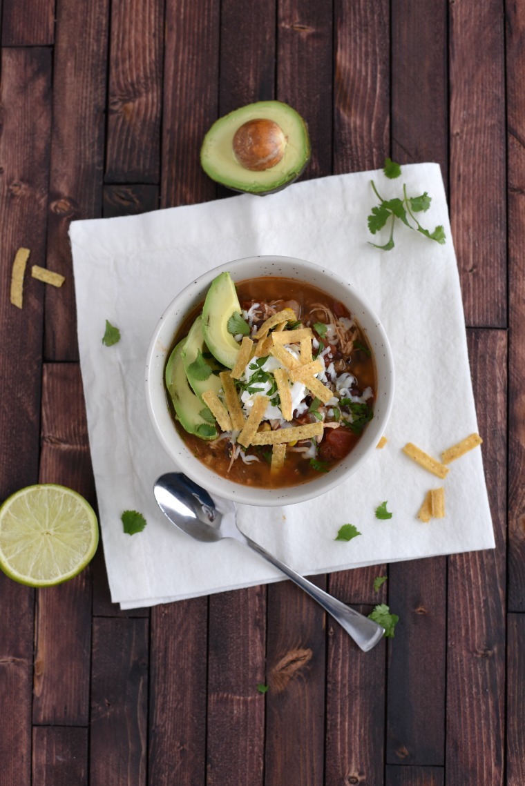bowl of enchilada soup on white napkin. Topped with tortilla strips, cilantro, and avocado