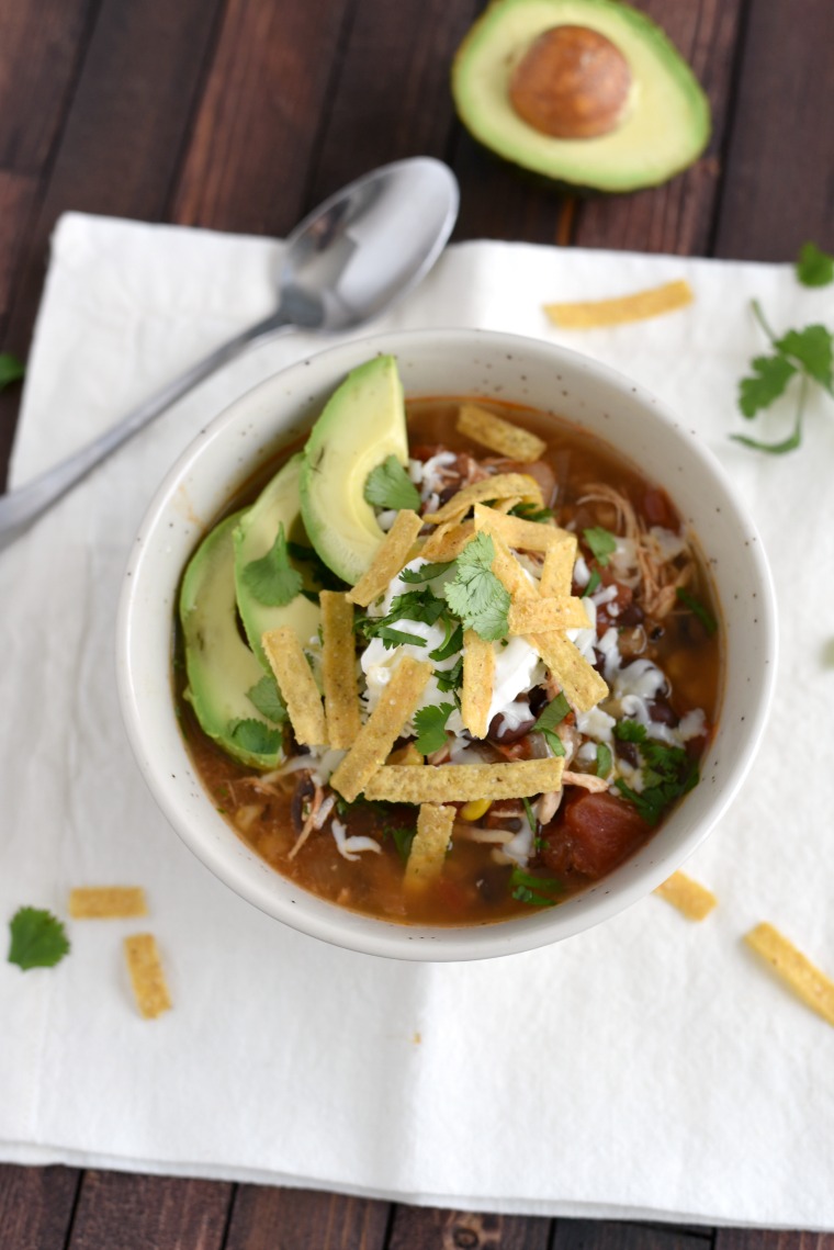 bowl with enchilada soup topped with sour cream, tortilla strips and sliced avocado 