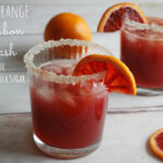 Two clear tumbler glasses rimmed in sugar with a blood orange garnish and filled with a red/orange cocktail and ice. Text overlay "Orange bourbon smash with vanilla bean sugar"
