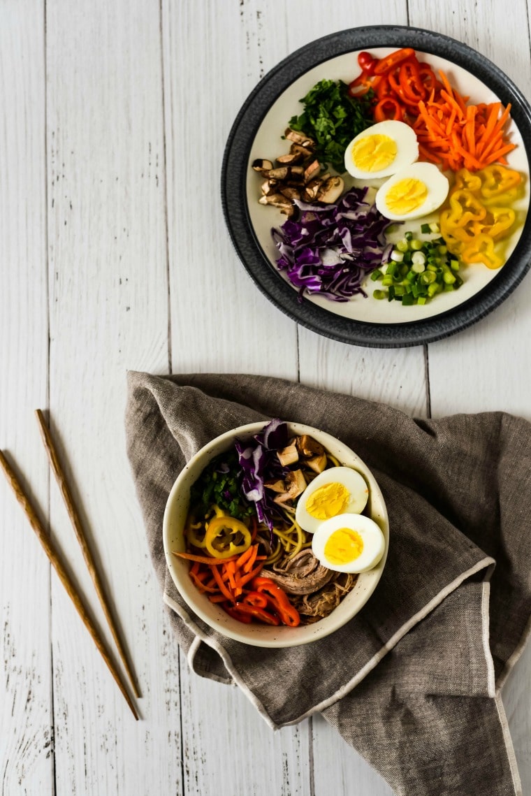 A bowl of ramen and chopsticks beside a bowl or ramen toppings
