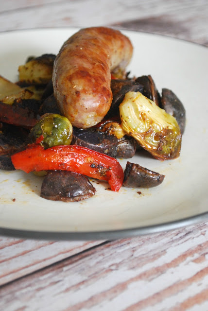 roasted potatoes, brussels sorouts, peppers and brats on white plate