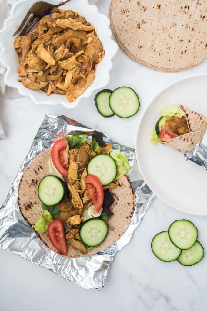 chicken shawarma being assembled on plates with ingredients scattered all around