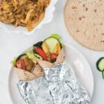 two chicken shawarma wrapped in foil on plate surrounded by ingredients