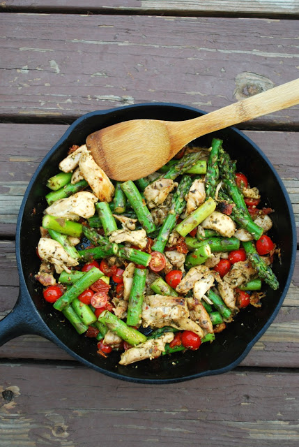 A cast iron skillet filled with skillet pesto chicken and veggies with a wooden spoon