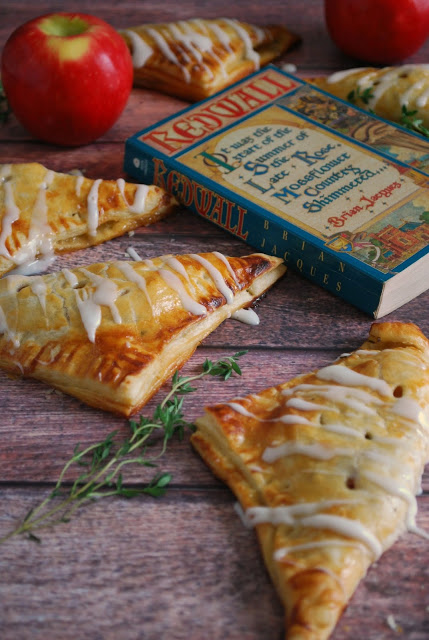 A wooden table with apple turnovers and a book and apple in the background 