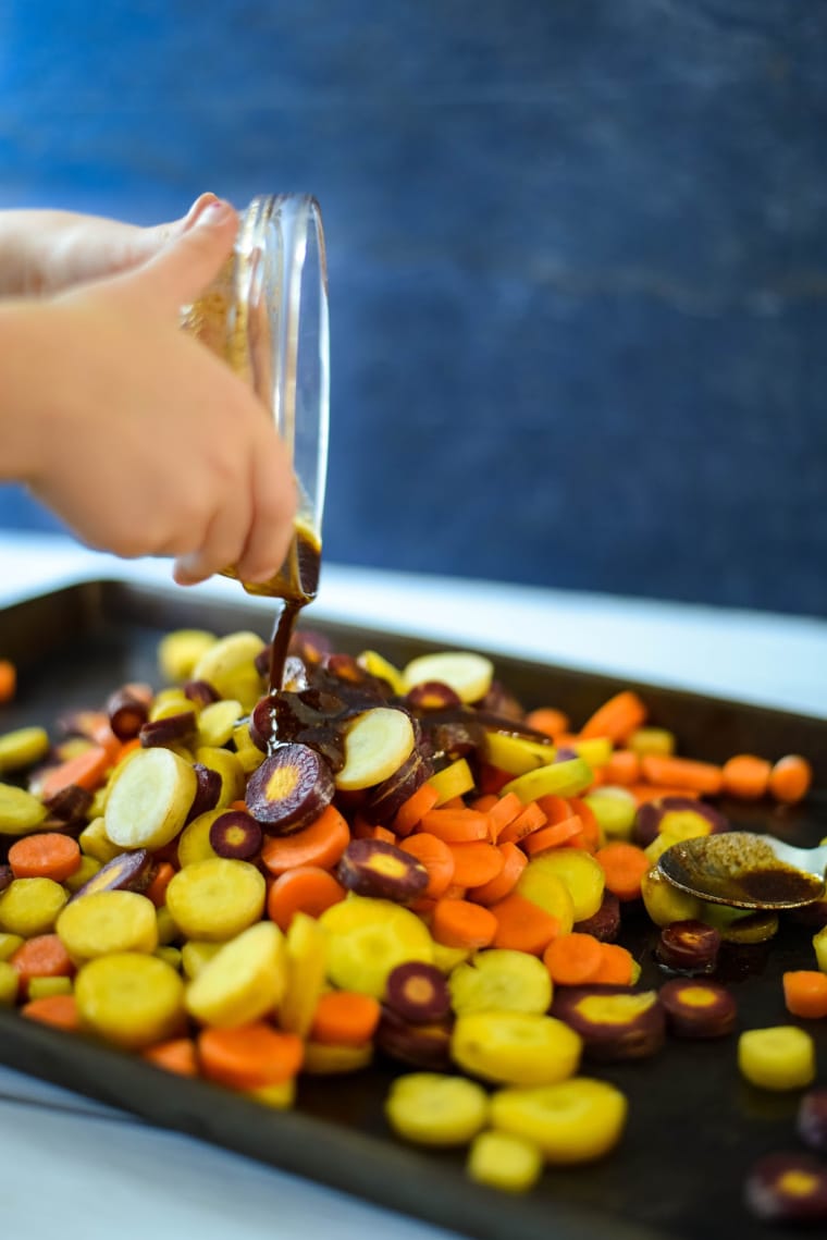 child pouring spices on rainbow carrots to roast