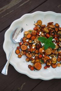 A white bowl with roasted rainbow carrots, a sprig of mint, and feta cheese