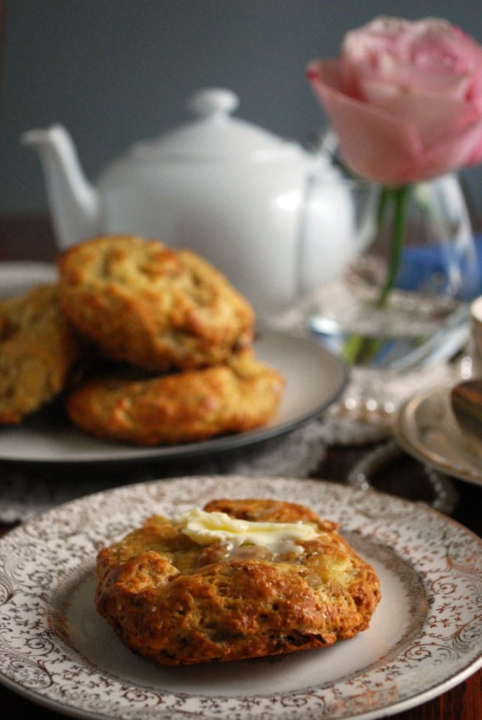 Two plates of apple bacon cheddar scones with a pink rose and a white teapot in the background 