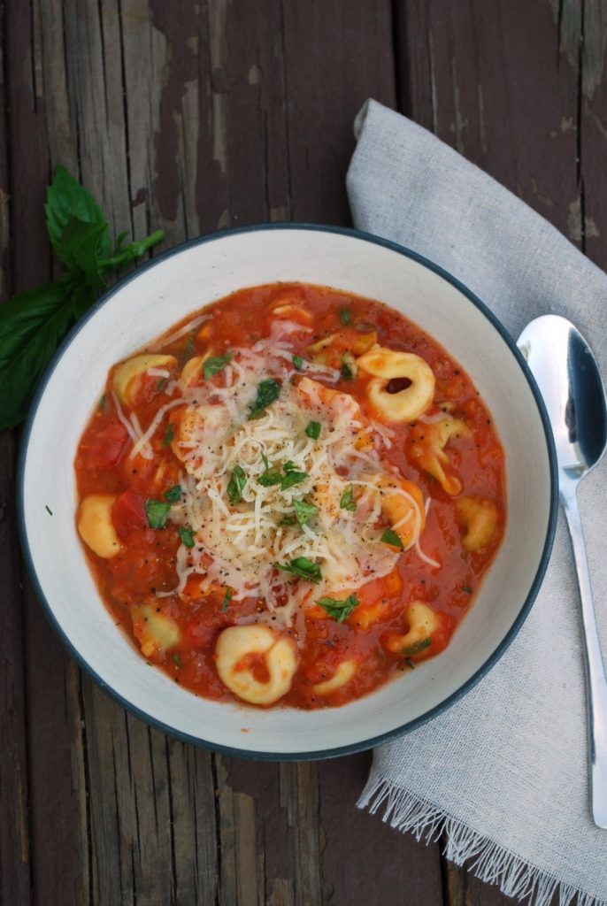 overhead view of bowl of tomato soup with cheese tortellini and basil 