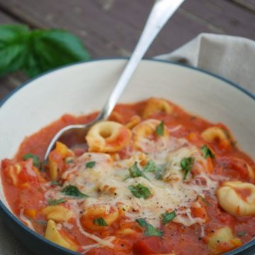 tomato basil soup with cheese tortellini in bowl with spoon, topped with cheese and fresh basil