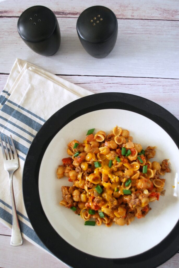 A plate of cheeseburger mac & cheese on a white wooden table with a blue striped napkin and a fork