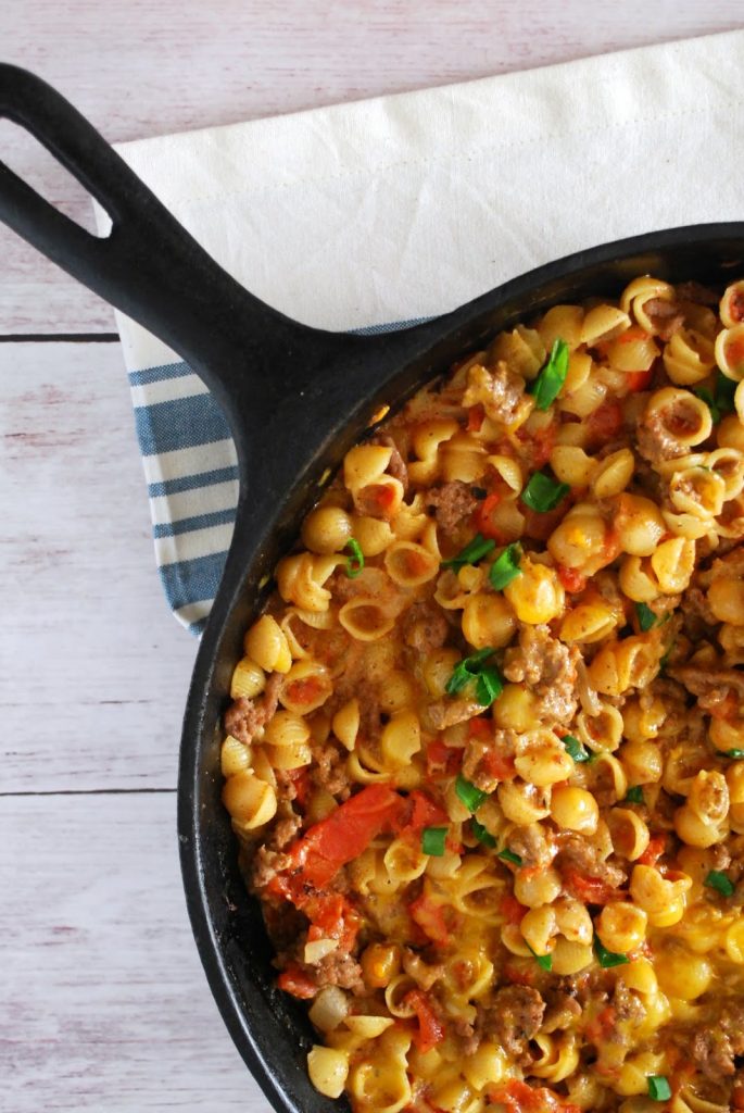 A cast iron skillet withe cheeseburger mac & cheese on a wooden table with a blue striped napkin