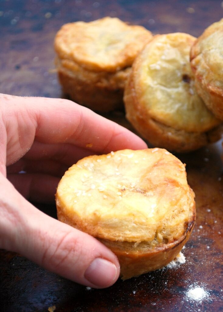 A Caucasian woman’s hand picking up a beef hand pie