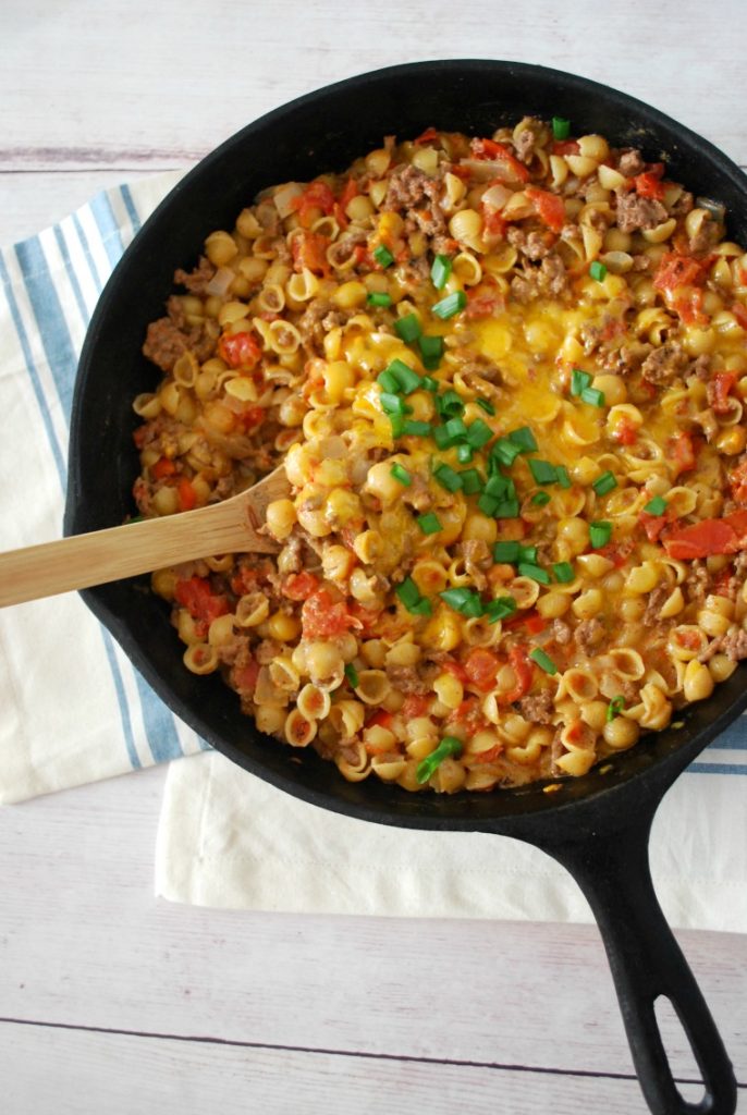 A cast iron skillet with a wooden spoon stirring cheeseburger mac and cheese