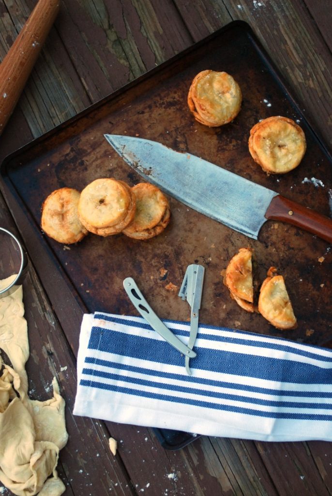 A wooden table topped with a knife, a blue and white napkin, and several beef hand pies