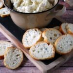 A board with a bowl of cheese spread and slices of bread