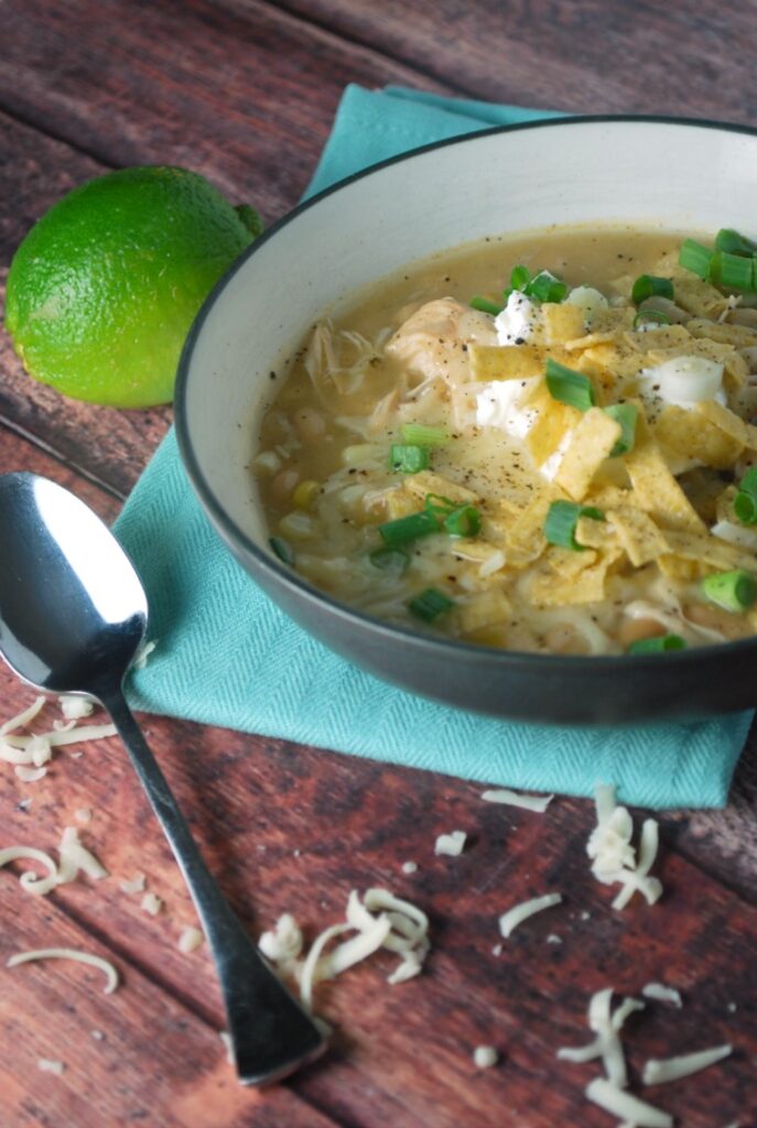 A bowl of chicken chili on a wooden table with a spoon and a blue napkin