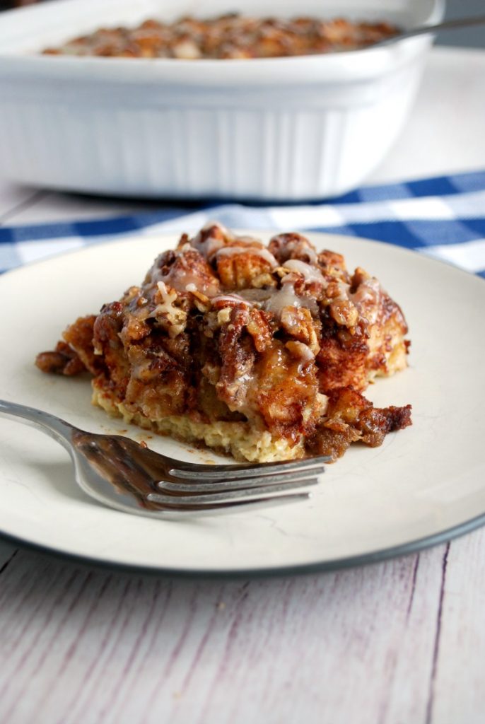 A piece of cinnamon roll breakfast casserole on a white plate with a fork
