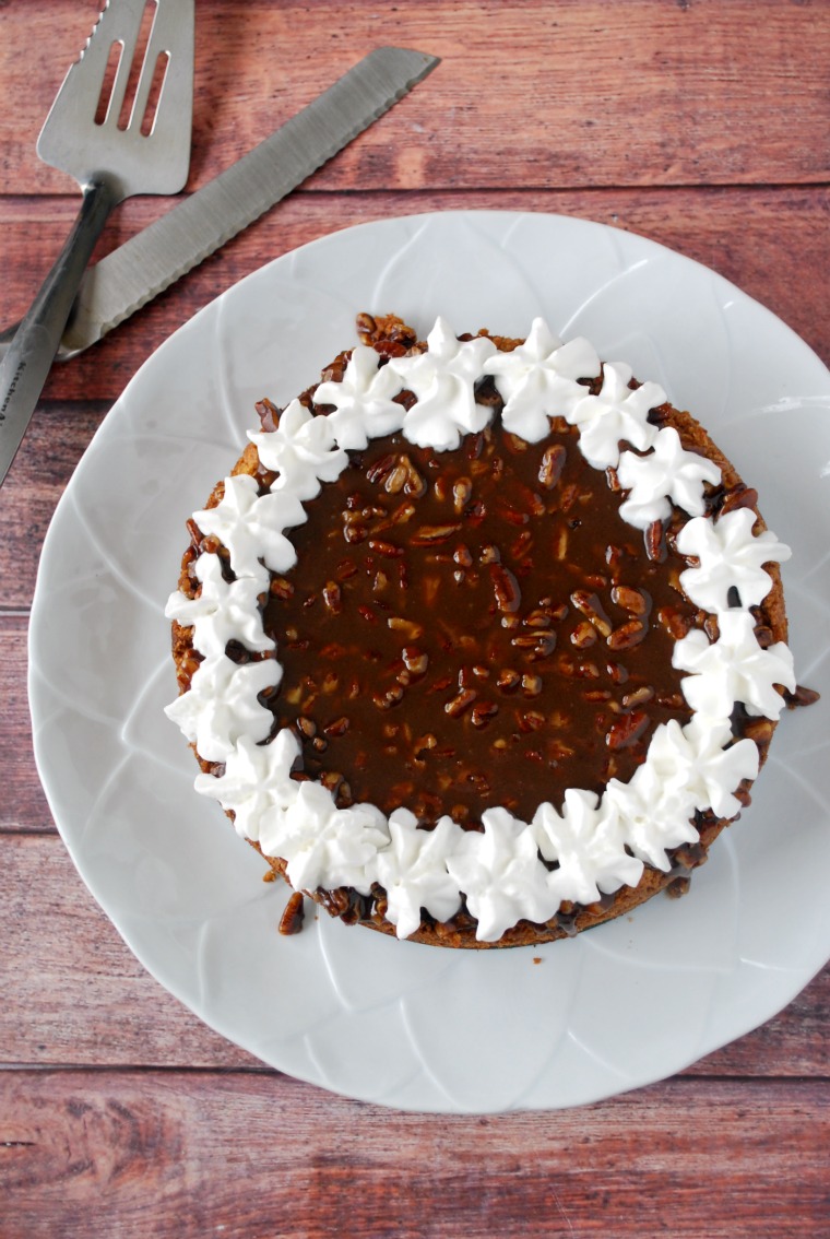 A white plate with a pumpkin praline cheesecake topped with whipped cream stars in a ring around the edge