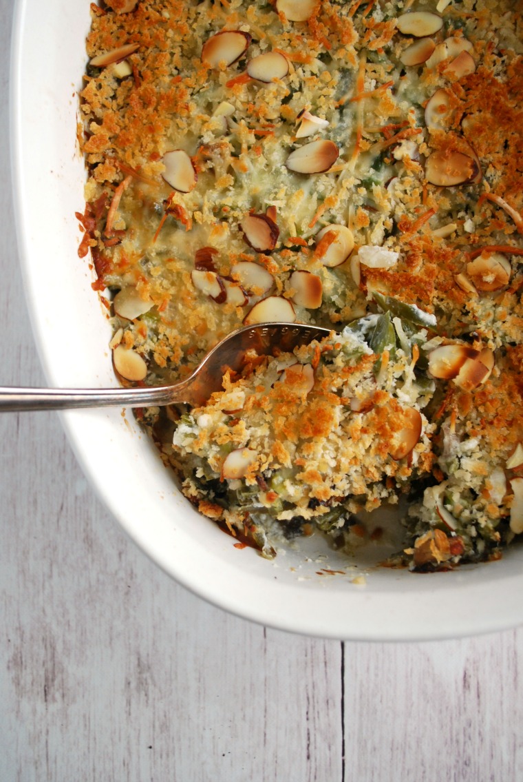 A spoon scooping up a serving of green bean casserole out of a white to serving dish