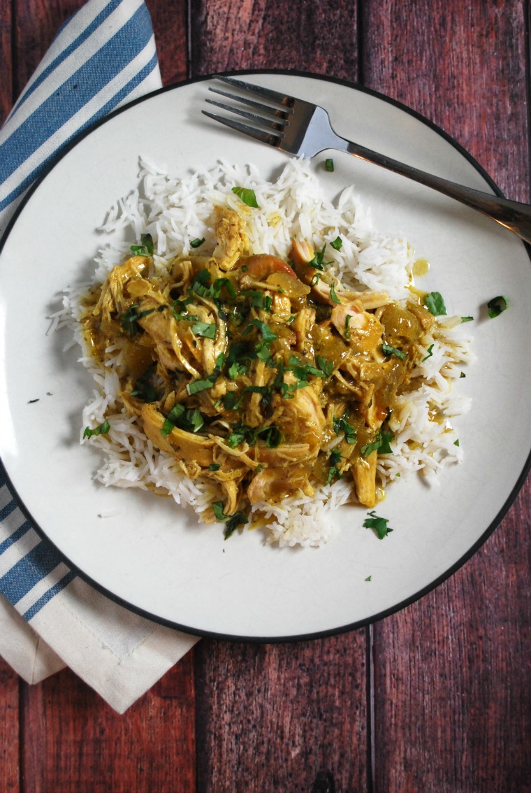 A white plate with rice and coconut chicken curry with a fork on a wooden table with a blue and white striped napkin