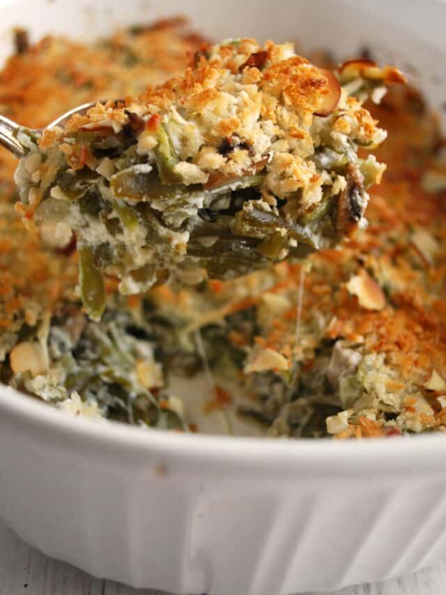 A spoon holding up a bite of green bean casserole over a white to serving dish of green bean casserole