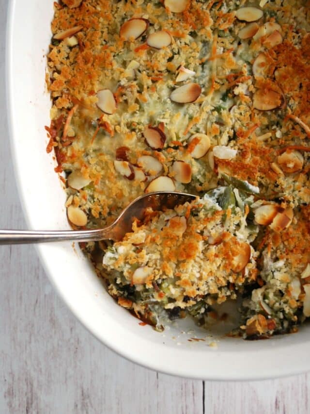 A spoon scooping up a serving of green bean casserole out of a white to serving dish