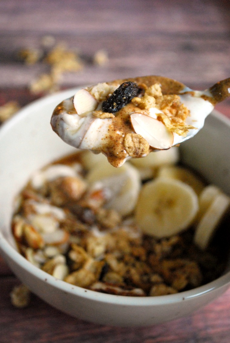 A spoon lifting a bite of granola and yogurt parfait out of a white bowl