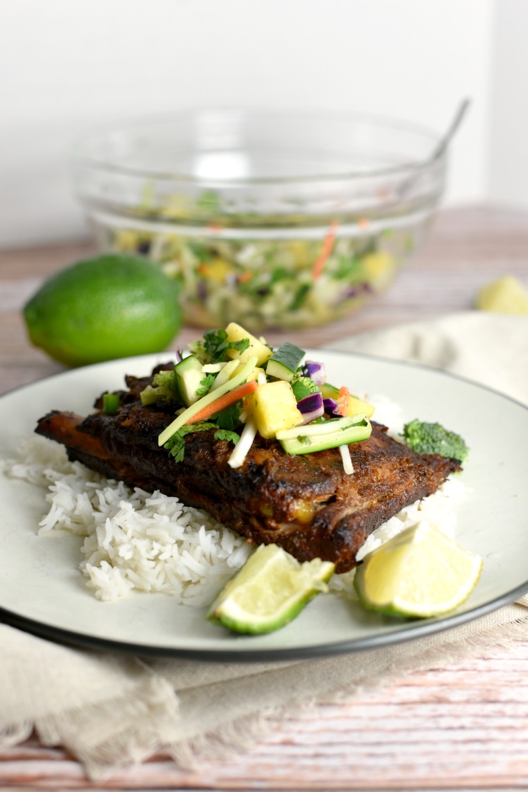 A white plate with Thai turmeric ribs and a bowl of pineapple slaw in the background 