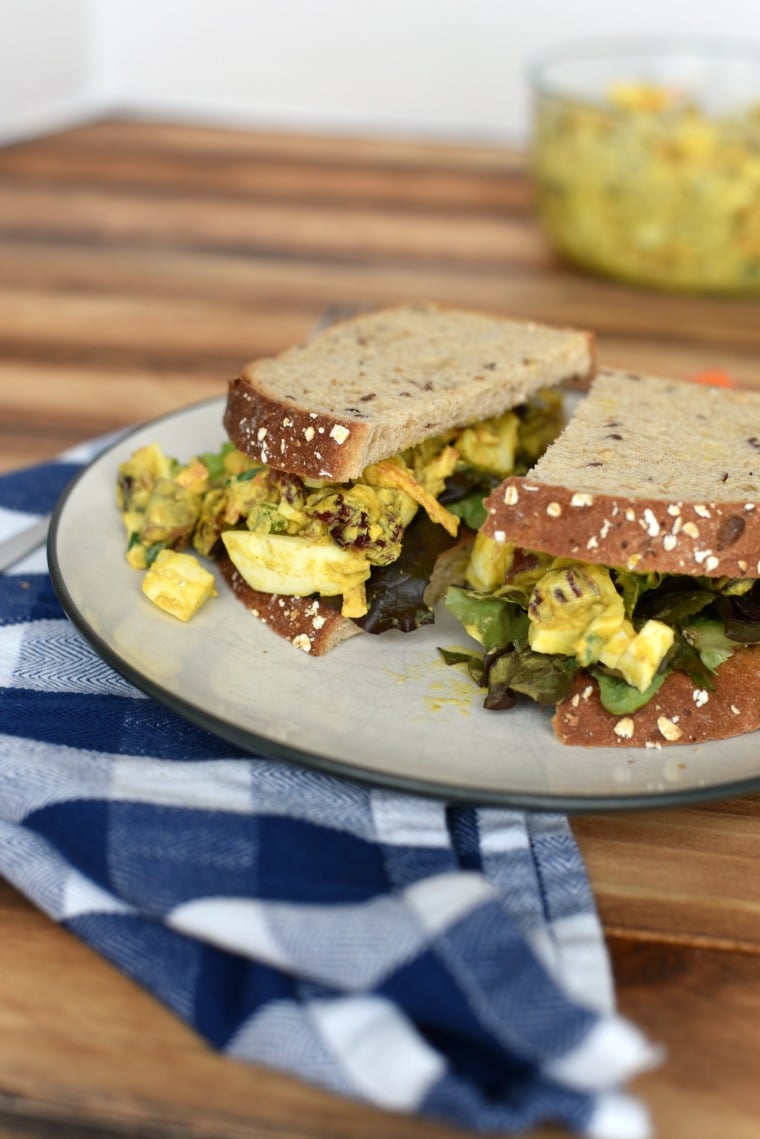 A white plate of egg salad sandwich on a wooden table 