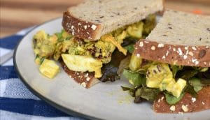 A curried egg salad sandwich with lettuce on a white plate on a wooden table