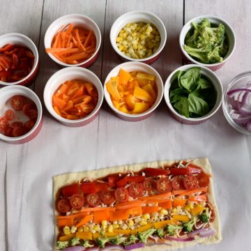 A rainbow veggie pizza with ramekins of colorful veggies