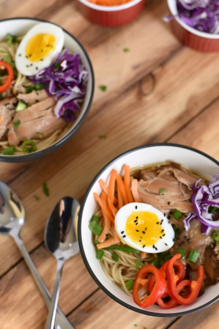 Two bowls of crock pot chicken ramen and two spoons on a wooden table