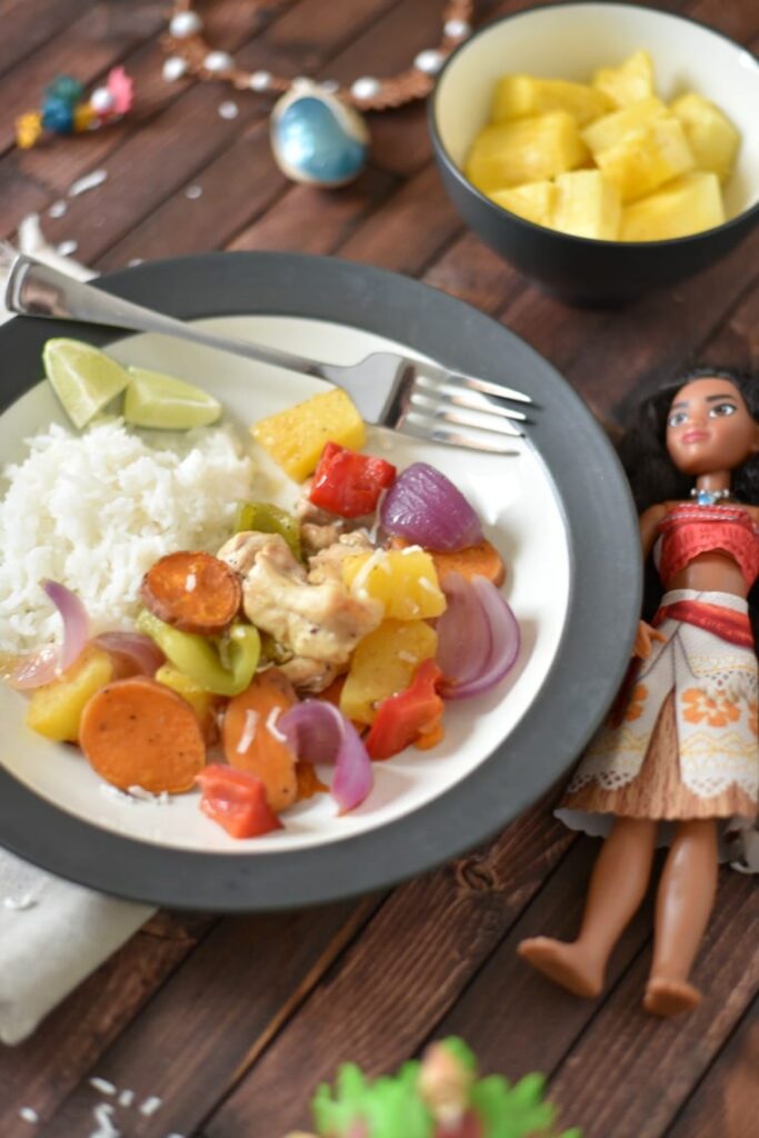 A black and white bowl of Polynesian chicken with a Moana doll on a wooden table