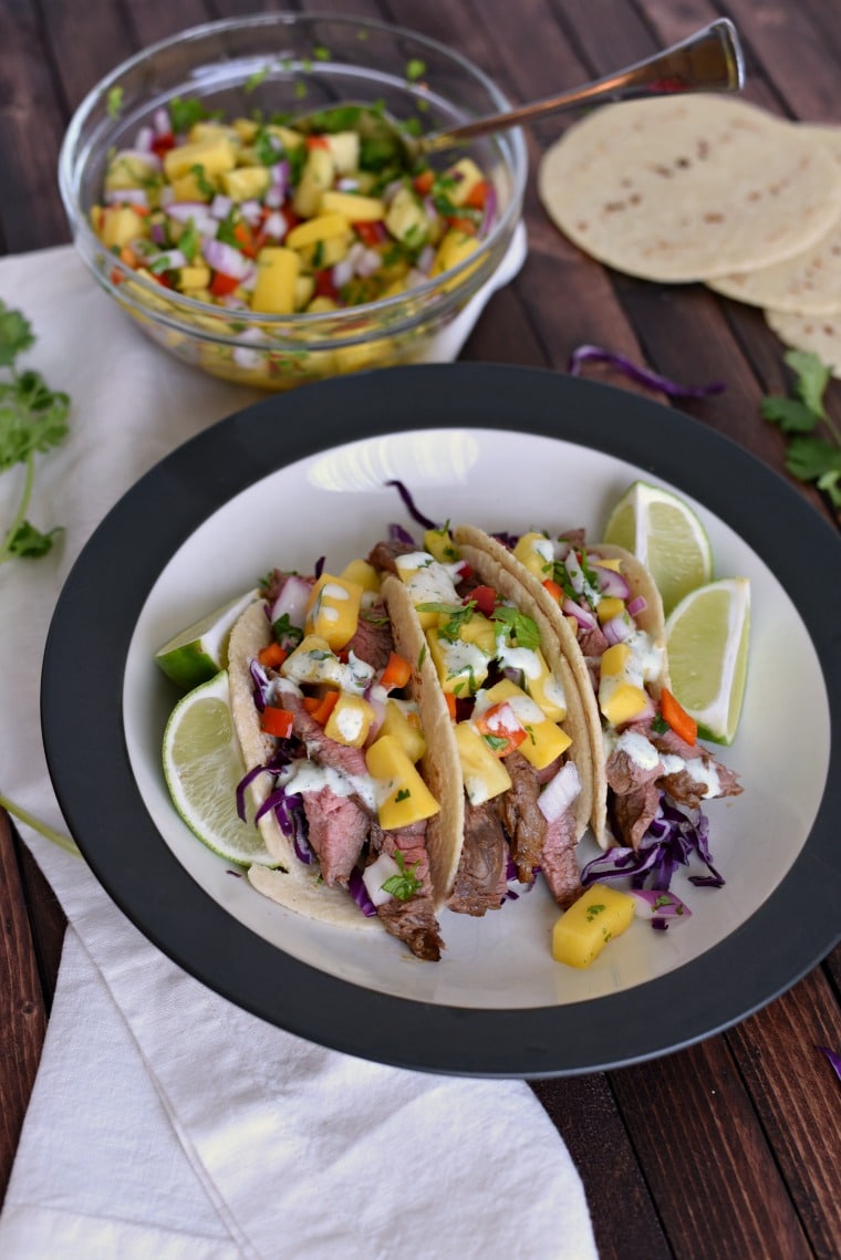 plate with tacos filled with pineapple salsa and drizzled with cilantro lime sauce. In background you can see a serving bowl with more salsa, and tortilla shells