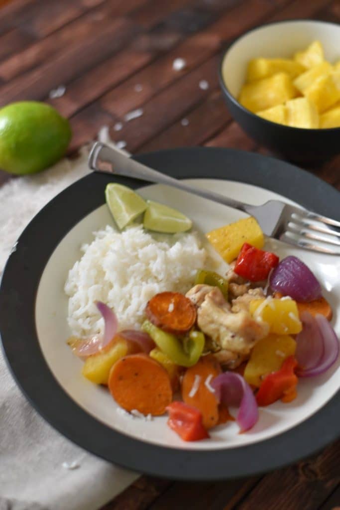 A black and white bowl of Polynesian chicken with a bowl of pineapple on a wooden table