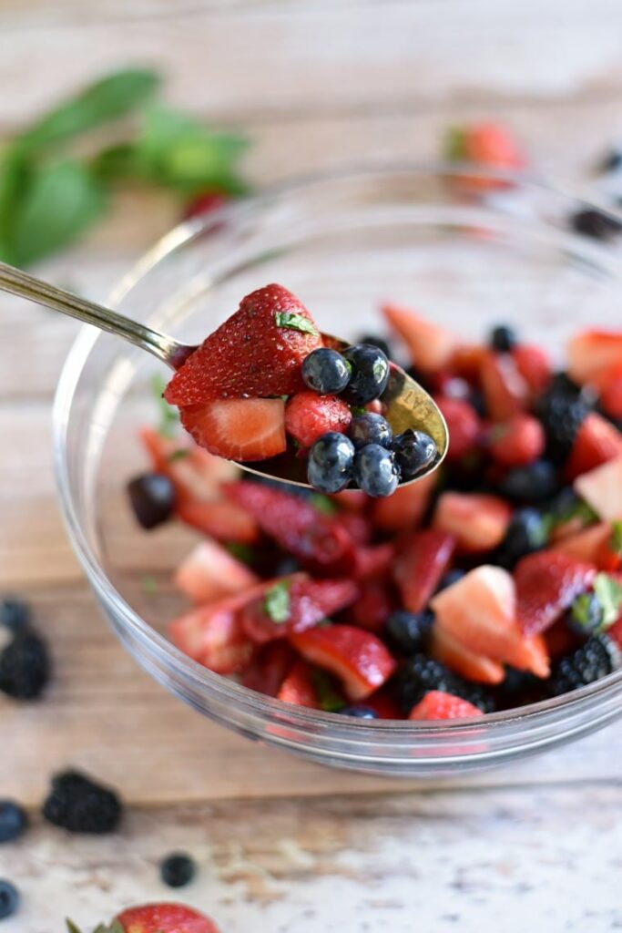 A silver spoon holding berry fruit salad over a clear bowl